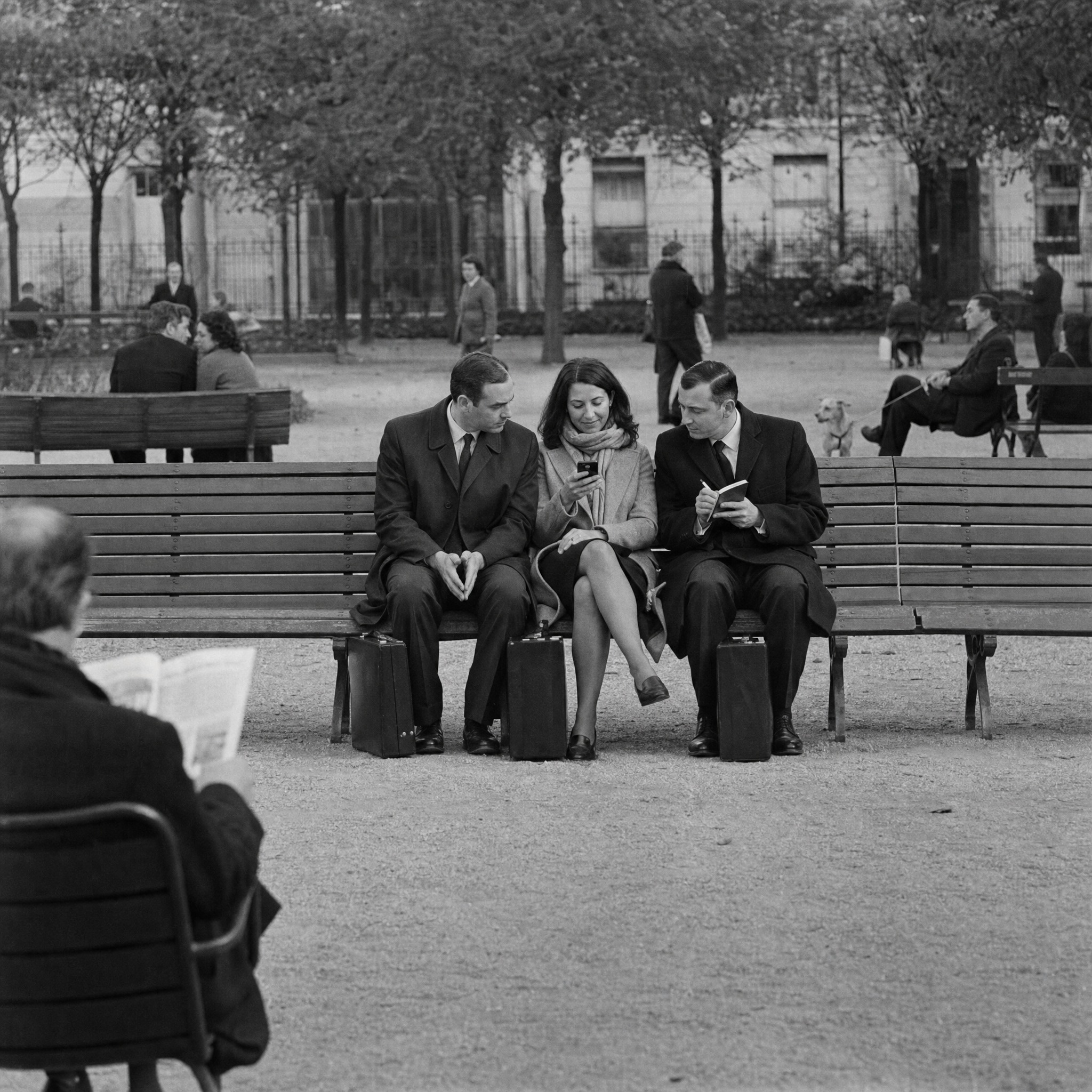 Three office workers on a park bench looking at a phone
